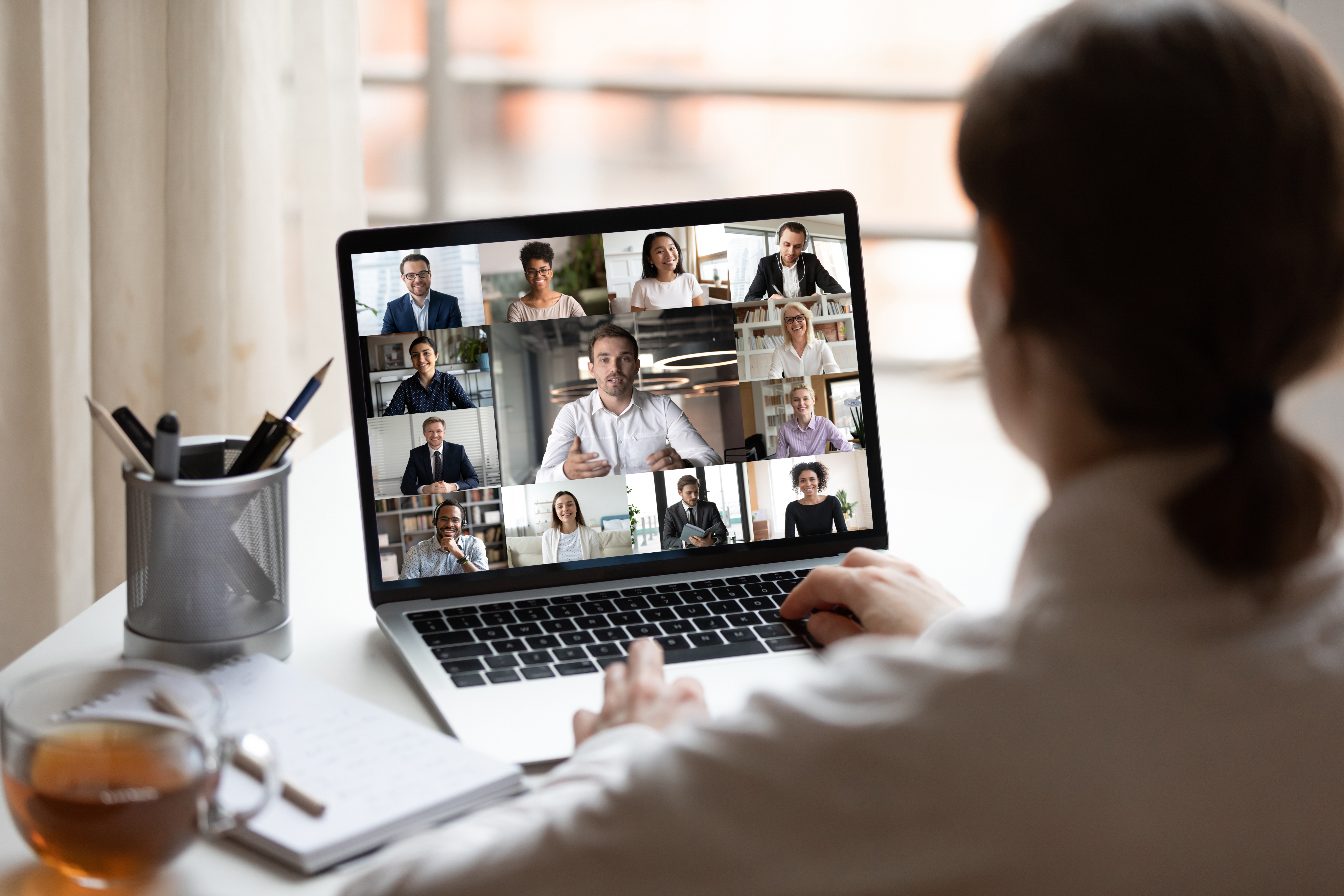 View over woman's shoulder of laptop screen with zoom meeting taking place.